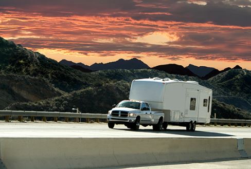 A car towing a trailer on a road at sunset